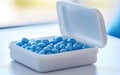 A close-up view of a white pill container filled with blue tablets on a surface in a bright room during the daytime Royalty Free Stock Photo