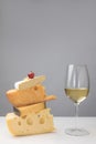 Close up view of white wine glass and grape on stack of different types of cheese on gray Royalty Free Stock Photo