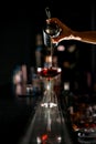 Close up view of woman bartender pours fine jet of red cocktail into drinking glass with ice standing on the bar counter Royalty Free Stock Photo