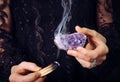 Close up view of woman in black lace dress, cleansing amethyst crystal cluster gemstone by smudging Palo Santo.