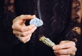 Close up view of woman in black lace dress, cleansing blue celestite crystal cluster gemstone by smudging white sage bundle.