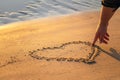 Close up view of woman hand drawing heart with finger on the sand at the beach. Romantic love symbol at tropical seashore at Royalty Free Stock Photo