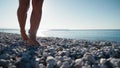 Close-up view of woman's legs walking on the pebble beach.