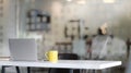 Close up view of workplace with tablet, office supplies and yellow coffee cup on white table with blurred office room