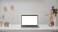 Close up view of  workspace with blank screen laptop, painting tools, wooden figure and decorations on white desk with white wall Royalty Free Stock Photo