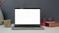 Close up view of workspace with open blank screen laptop, cup, glasses  and books on white table with grey wall Royalty Free Stock Photo