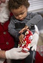 Young bi-racial child opening a Christmas present on Santa`s lap