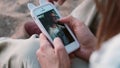 Close-up view of young couple sitting on the beach, on the sand and looking photos on smartphone, using touchscreen.