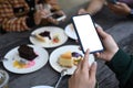 Young female using mobile phone taking photo of sweet dessert  during spending time with her friends at cafe. Royalty Free Stock Photo