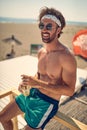 Close-up view of a young guy in swimsuite is sitting on the beach and posing for a photo. Summer, beach, sea Royalty Free Stock Photo