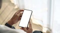 Close up view of man sitting near window and holding mock up smart phone with white screen. Royalty Free Stock Photo