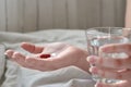 Close-up view of young woman`s hands. Girl in bed holding tablets or pills and glass of water. Painkiller with space for text Royalty Free Stock Photo