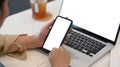 Young woman sitting in front of laptop computer and holding mobile phone with blank screen. Royalty Free Stock Photo