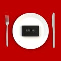 Close up of vintage black audio tape cassette on plate, knife and fork on red background