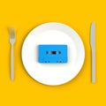 Close up of vintage blue audio tape cassette on plate, knife and fork on yellow background Royalty Free Stock Photo