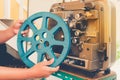 Close up of vintage classic mobile 8 mm or 16 mm movie film projector and hand holding empty film reel with vintage color style.