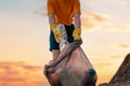 Close up of volunteer& x27;s hands in rubber gloves puts a dirty plastic bottle in bag with garbage. Sunset sky on the