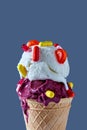 Cold delicious ice cream in a waffle cone with red and yellow pills and a lollipops against a blue background. Close-up. Royalty Free Stock Photo