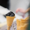 Close-up of waffle cone with ball of trendy black ice cream. Delicious cooling portion on hot day and just for fun