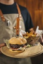 Close-up of a waiter using face mask serving a delicious meat burger with fries