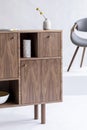 Close-up of a walnut sideboard with a vase standing in a white living room interior. Real photo