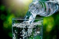 Close up of water flowing from drinking water bottle into glass on blurred green nature bokeh background with soft sunlight