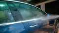 CLOSE UP: Water is sprayed over side of a blue car being washed in the driveway.