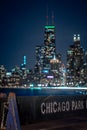 A close up of a weathered blue wooden Chicago Park District barricade with the city skyline and lights out of focus bokeh in the