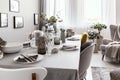 Well-laid table with plates and glasses in a grey dining room interior. Real photo