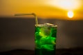 Close up wet glass of green cold mint drink, colorful orange sunset background on the terrace. Cooling summer drink. Summer fresh