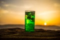 Close up wet glass of green cold mint drink, colorful orange sunset background on the terrace. Cooling summer drink. Summer fresh
