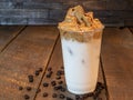 Close-up of Dalgona Whipped coffee in a plastic cup with milk on a wooden background.