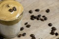 Close up of whipped instant coffee on a cup of milk on a crystal glass with coffee beans on a wooden surface. Dalgona coffee