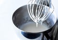 Close up of a whisk raised out of a metal mixing bowl dripping with royal icing.