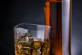 Close-up of whiskey with ice cubes in glass near bottle on black background, cold atmosphere Royalty Free Stock Photo