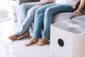 Close up of white air purifier on the floor in living room the background of young Asian couple relaxes on sofa. Concept of caring