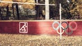 Close up on white bicycle sign or icon and colored sign of the Olympic rings on a brown wooden fence in the public park.