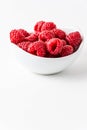 Close up of white bowl with red raspberries, selective focus, on white background in vertical Royalty Free Stock Photo