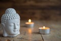 Close-up of white buddha figure and candles on weathered wooden table and dark background Royalty Free Stock Photo