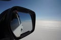 Close-up of a white car`s side-view mirror reflecting the view back of the vastness of the Uyuni Salt flats, Bolivia