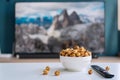 Close up of a white ceramic bowl of caramel popcorn and remote control for smart TV. Home cinema and watching a movie or series
