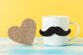 Close up of white ceramic cup with a felt moustache and sparcle golden heart on yellow background. Copy space Royalty Free Stock Photo