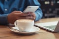 Close up white coffee cup with latte art on wood table on background is blurred with the businessman using the phone at coffee