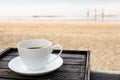 Close up white coffee cup on wood table at sunrise sand beach in the morning