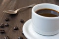 Close-up of white cup with coffee and spoon, on wooden table with coffee beans Royalty Free Stock Photo