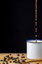 Close-up white cup with falling coffee, coffee beans and wooden spoon, on rustic table and black background, vertica Royalty Free Stock Photo