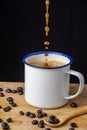 Close-up white cup with falling coffee, coffee beans and spoon on wooden table and black background Royalty Free Stock Photo