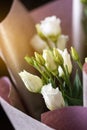 Close up of white eustoma flowers in a bouquet wrapped in pink paper.