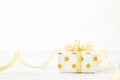 Close up of white gif box with golden star pattern and gold ribbon bow on bokeh background