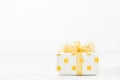 Close up of white gif box with golden star pattern and gold ribbon bow on bokeh background